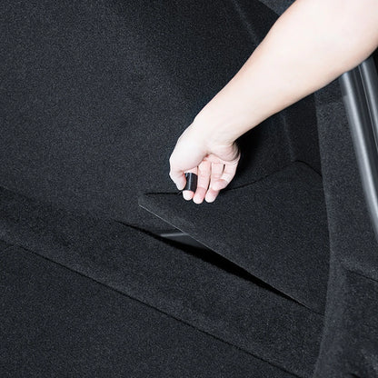 Hand lifting the carpet lid of Tesla Model 3 Highland trunk side storage box