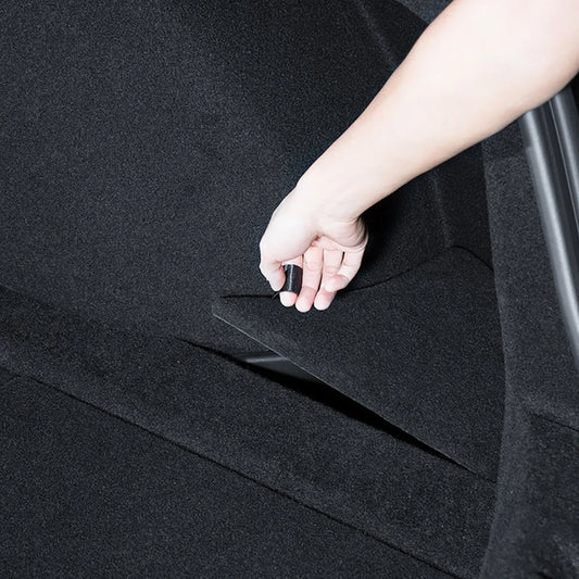 Hand lifting the carpet lid of Tesla Model 3 Highland trunk side storage box